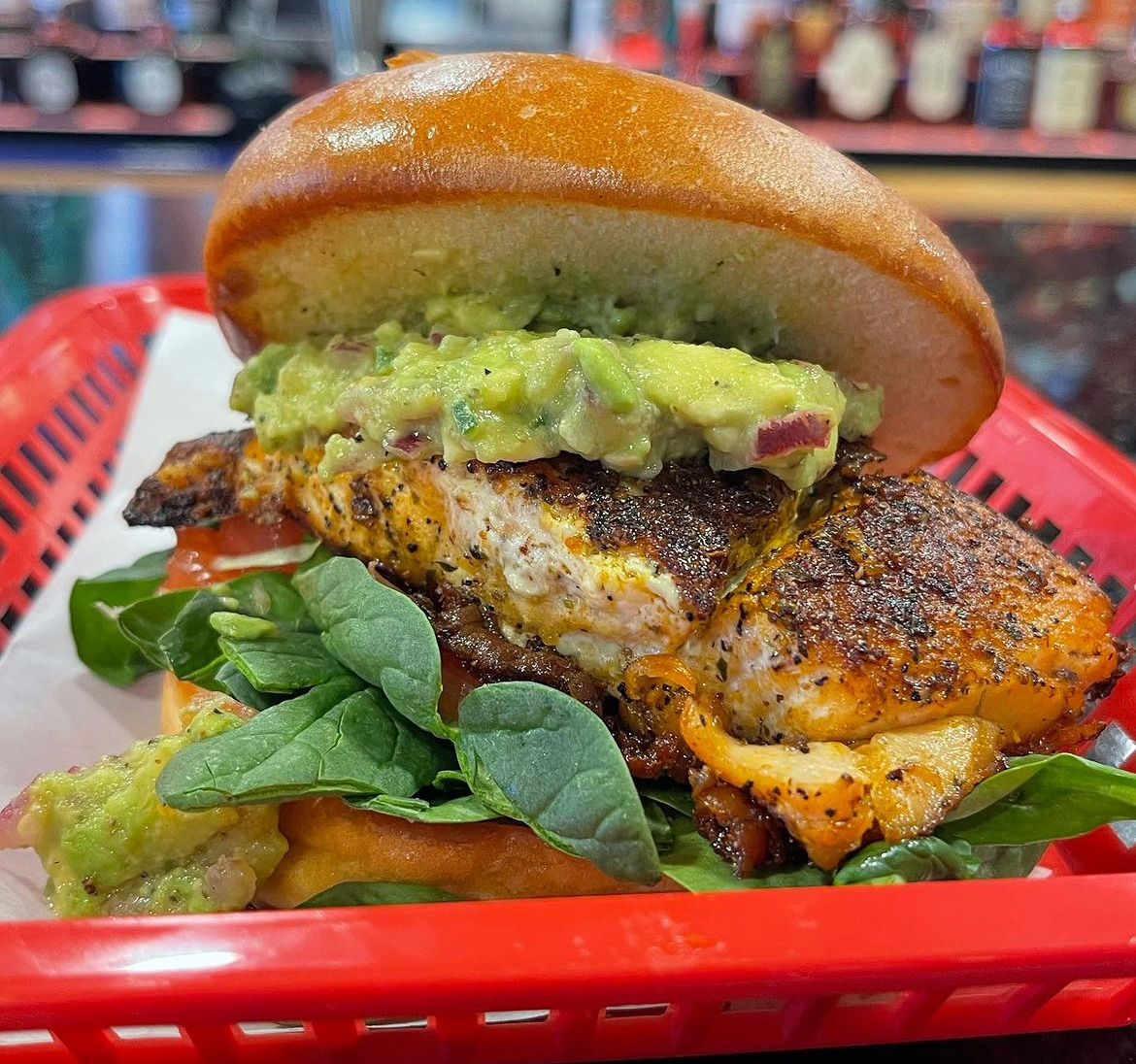 Blackened salmon burger with avocado and spinach in a red basket